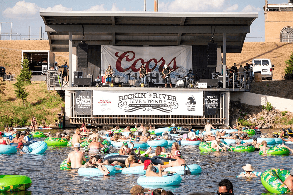 People tubing on the trinity river in front of band at panther island pavilion